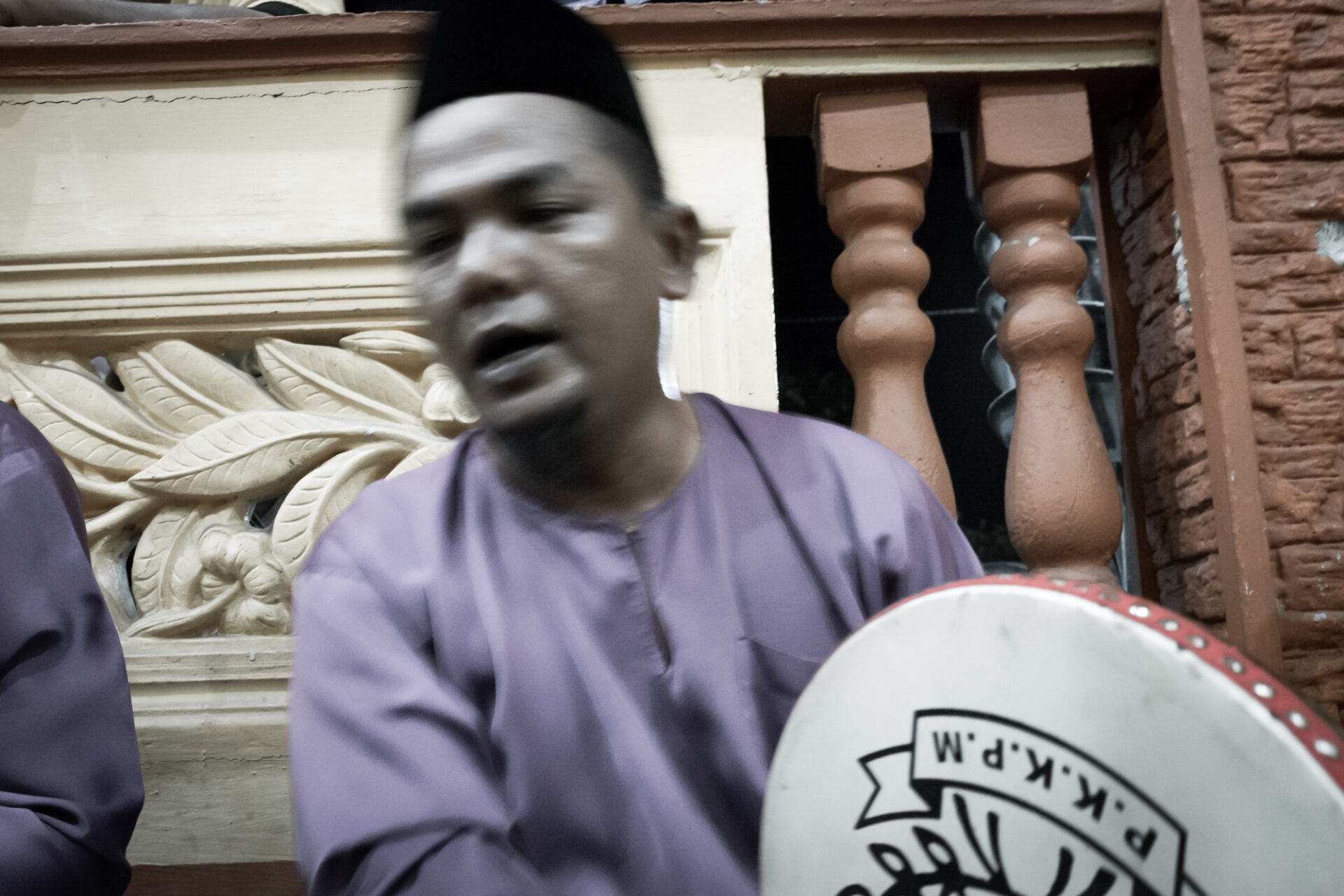 A man during Kompang Jidor performance, pillars behind